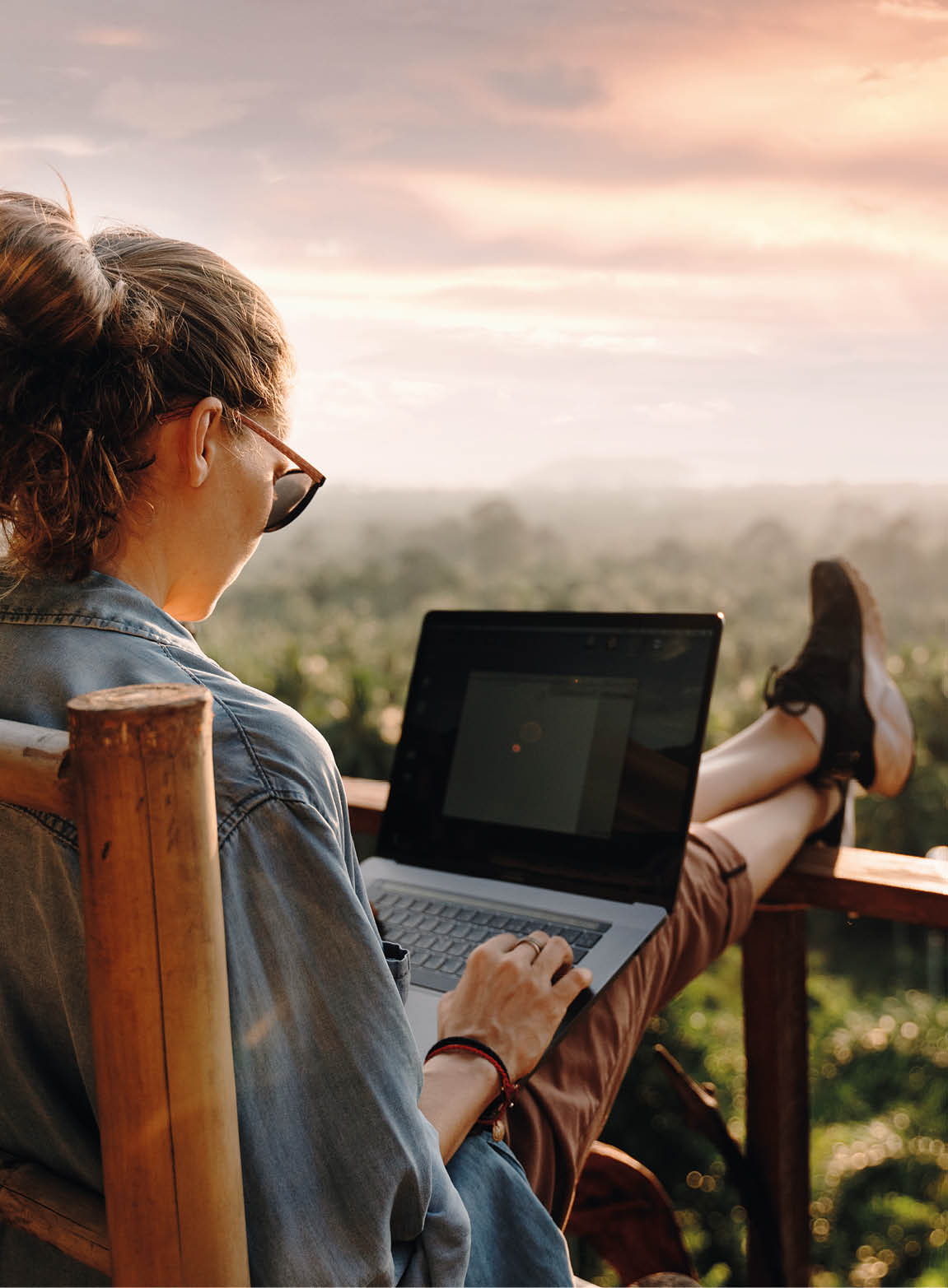 Young business woman working at the computer in cafe on the rock. Young girl downshifter working at a laptop at sunset or sunrise on the top of the mountain to the sea, working day.