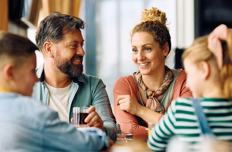 Happy parents communicating with their children while having a meal in a restaurant.